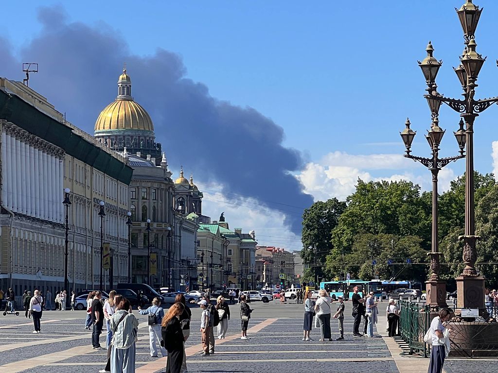 Pedestrians stand in front of St. Isaac's Cathedral in central St. Petersburg as a plume of black smoke rises in the distance after the drone strike.